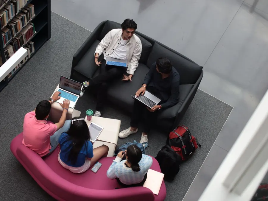 Students studying together on sofas and at laptops in a library, seen from above