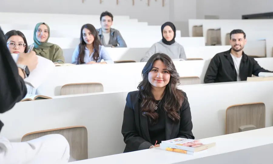 A smiling student in a lecture hall with classmates seated behind her