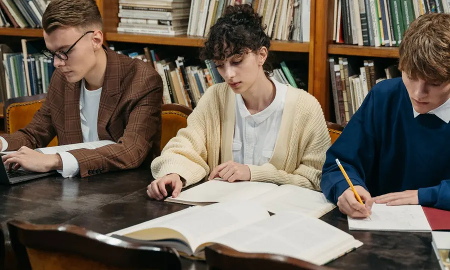 Three students studying with open books at a library table